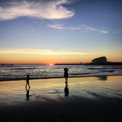 Silhouette people on beach against sky during sunset