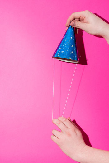 Cropped hands holding party hat against pink background