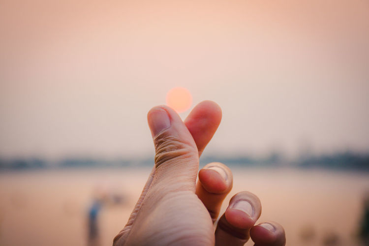 Close-up of human hand against sky during sunset