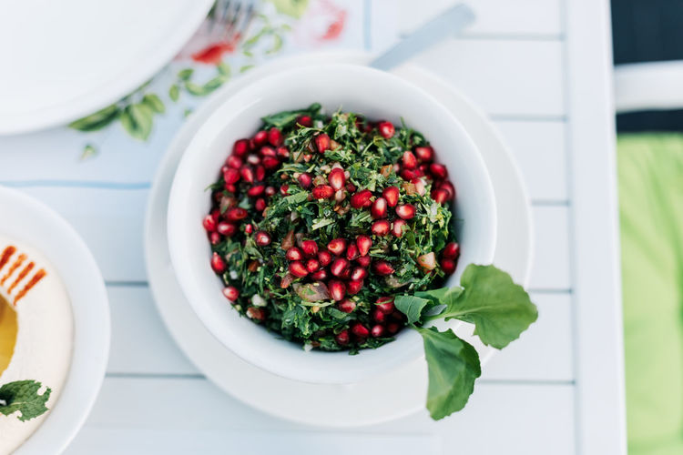 On the table in an arab restaurant there is a parsley tabbouleh salad with pomegranate seeds. 