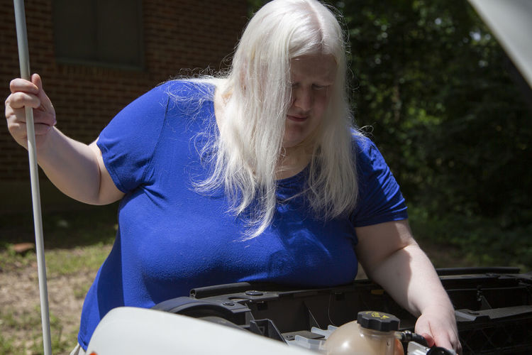 Woman checking car engine while standing outdoors