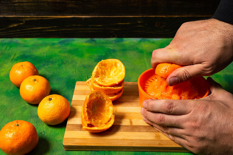 Cropped image of hand holding orange fruits on cutting board