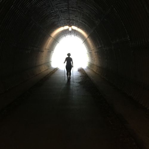 Rear view of silhouette woman with hiking poles walking in tunnel