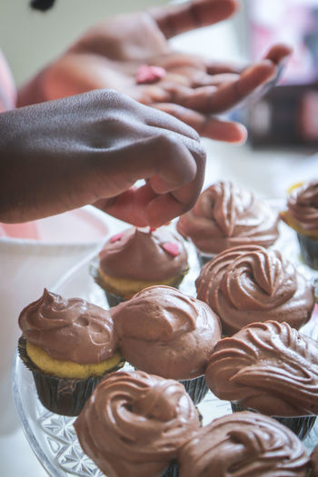 Cropped hands of child garnishing cupcakes on table