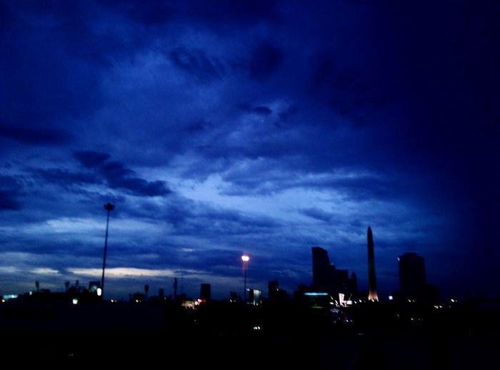 Illuminated cityscape against cloudy sky at dusk