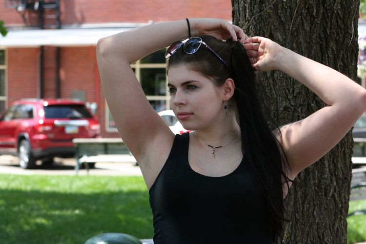 Young woman looking away while standing against tree at park