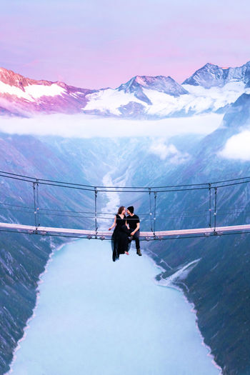 Couple sitting on bridge against sky