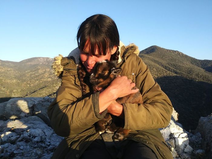 Woman embracing goat against mountains