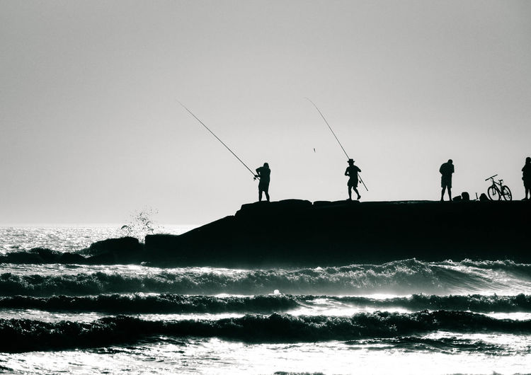 Silhouette men fishing by sea against sky