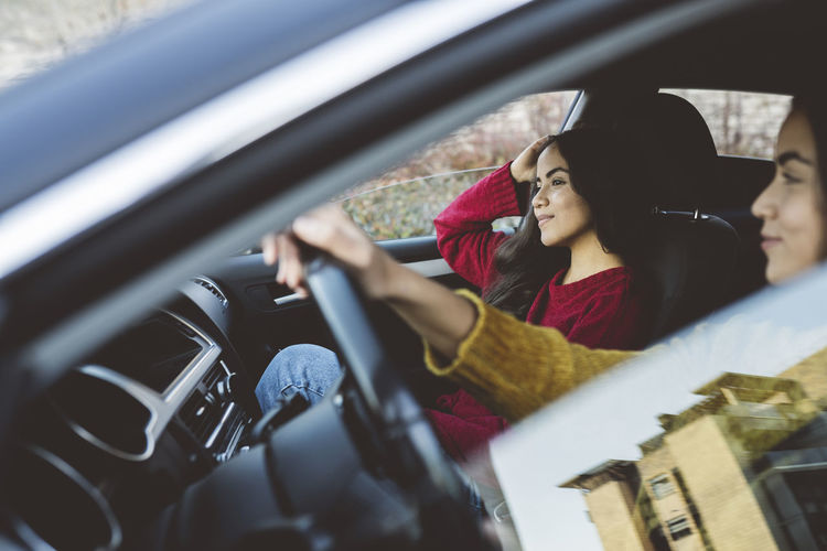Thoughtful young woman sitting with sister driving car on road trip
