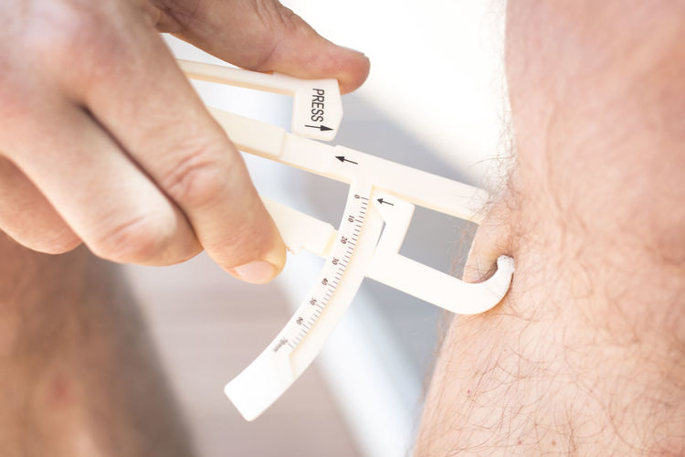 Midsection of man checking leg fat with caliper