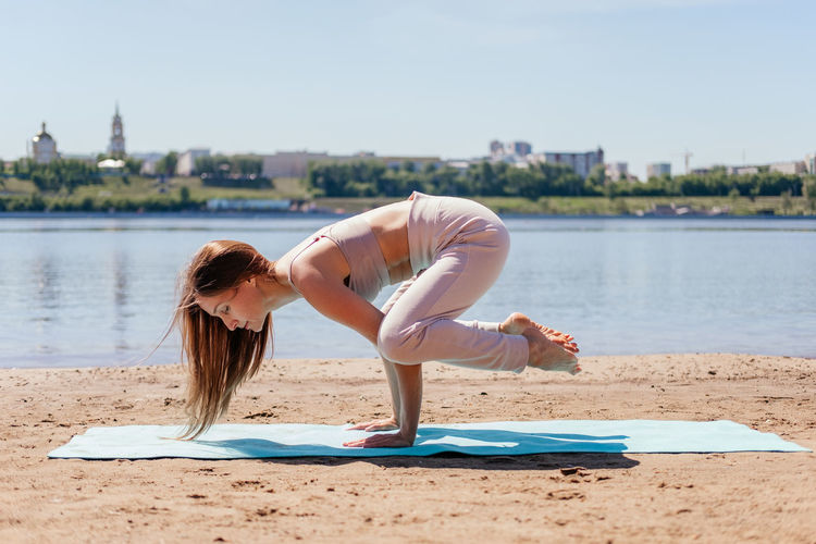 Middle aged woman in sportswear balancing on hands in bakasana yoga pose on sand. stretching woman