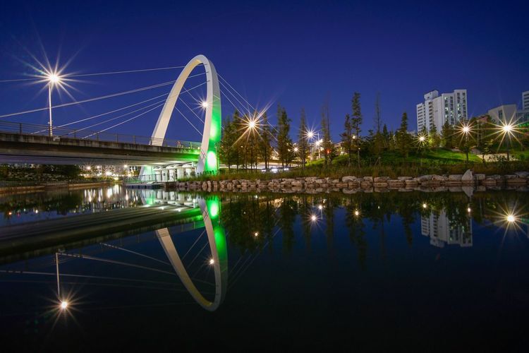Illuminated bridge over river in city at night