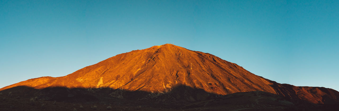 Scenic view of volcano against clear blue sky at sunrise