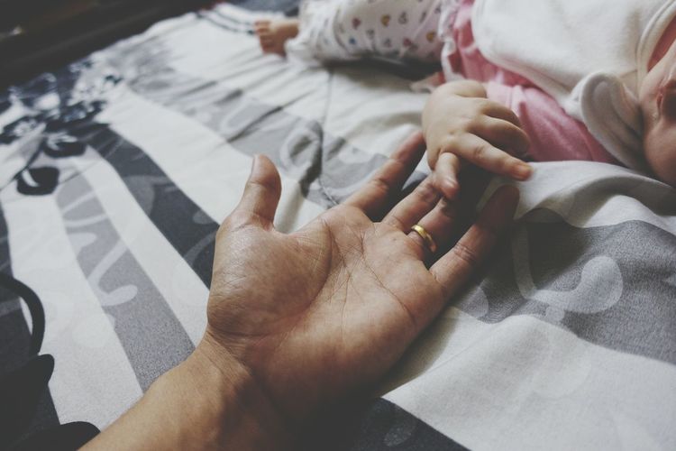 Baby holding father hand on bed at home