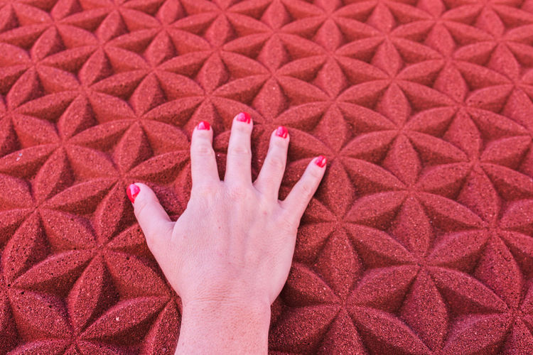 Cropped hand of woman touching patterned red wall