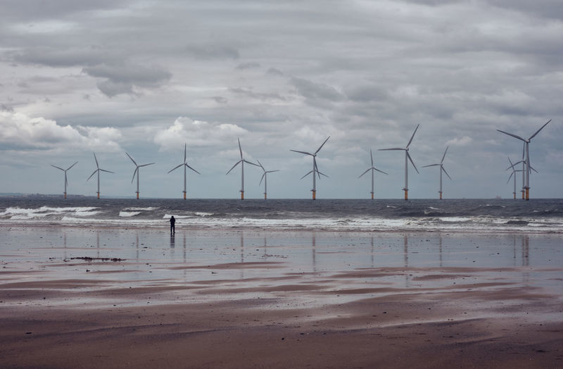 Windmills on beach against sky