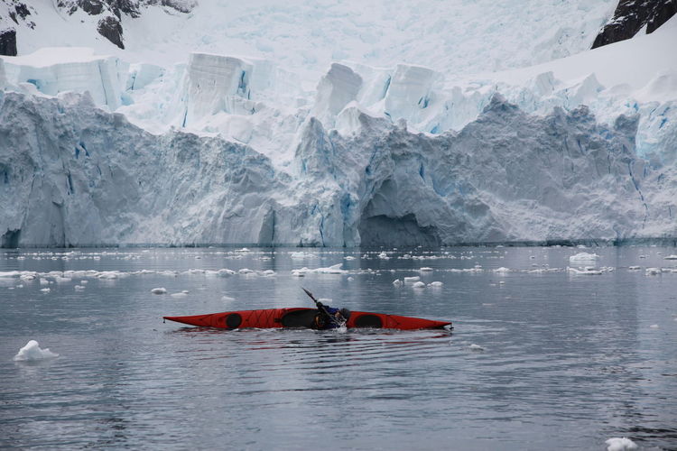 Person practicing rolling kayak in river against glacier