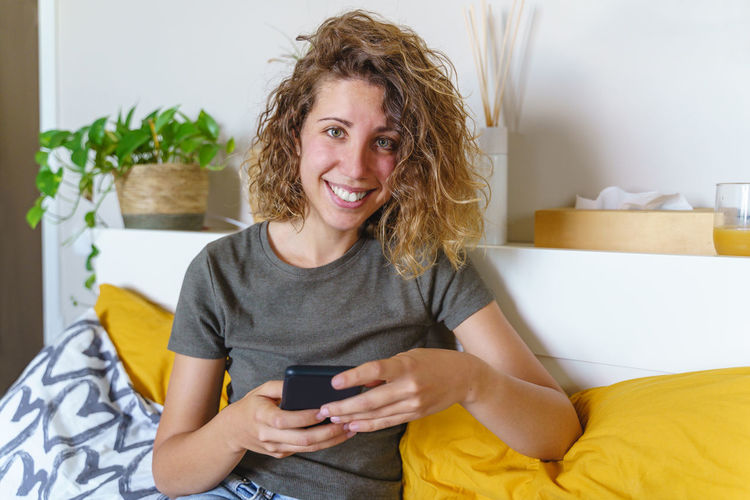 Portrait of smiling young woman using mobile phone at home