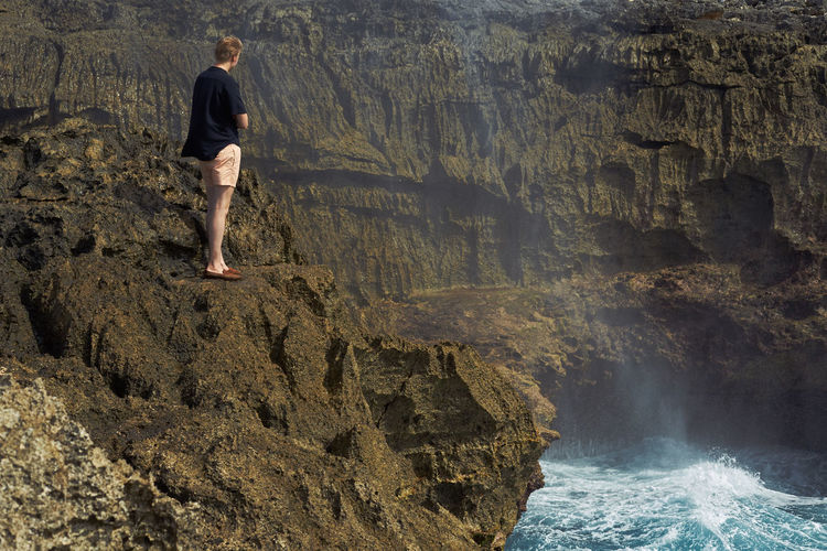 Rear view of man standing on rock by sea