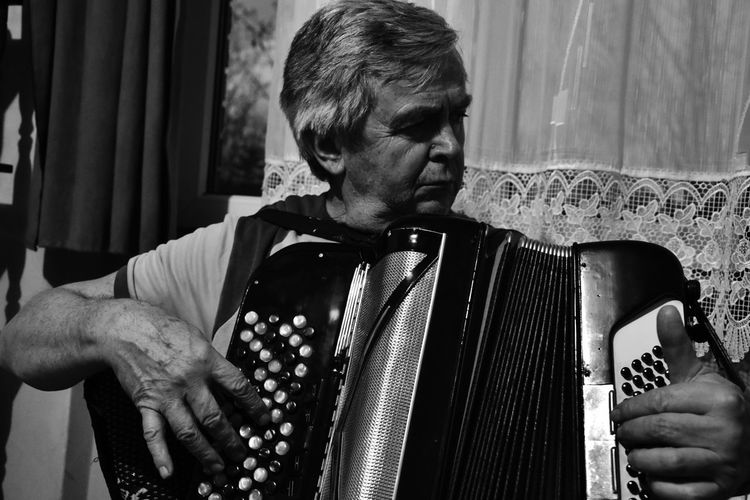 Senior man playing accordion while sitting at home