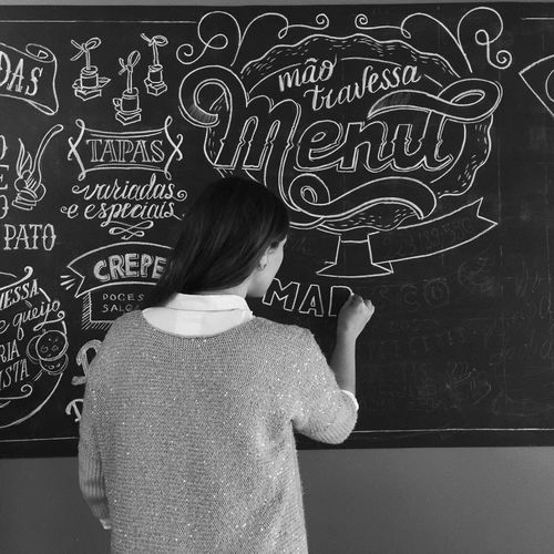 Rear view of woman writing on blackboard