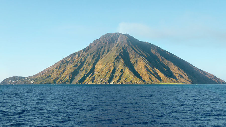 Scenic view of sea and volcano against clear blue sky