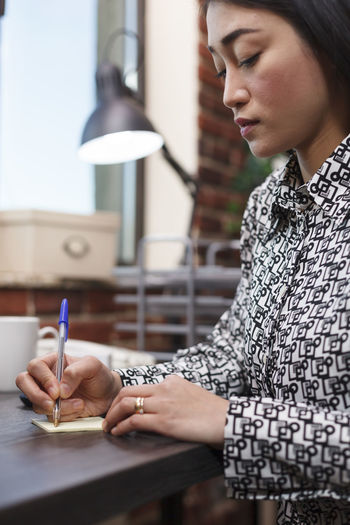 Woman writing on adhesive note at table