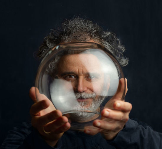 Man with curls beard silver-colored mustache holds transparent glass ball his hands looks through