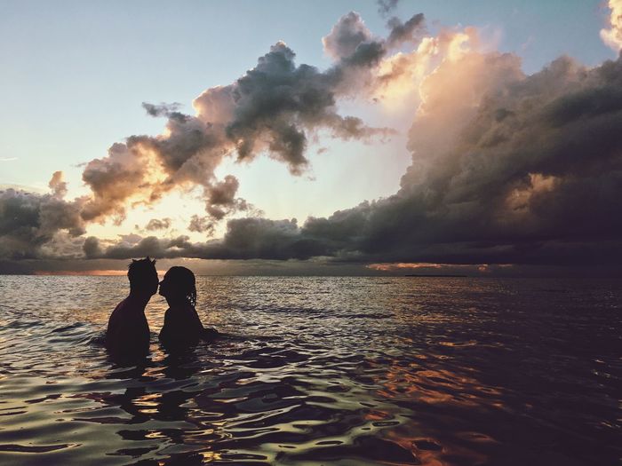 Silhouette couple in sea against sky during sunset
