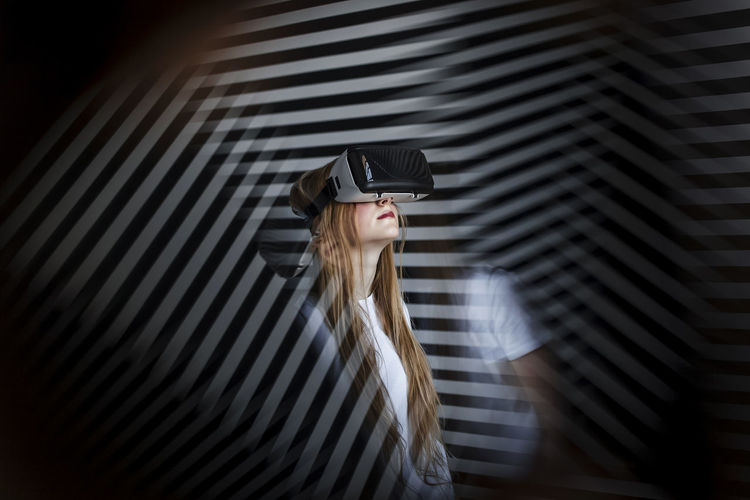 Girl with blond hair wearing virtual reality headset by striped wall