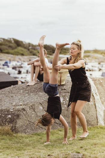 Mother helping daughter to do handstand on land at harbor