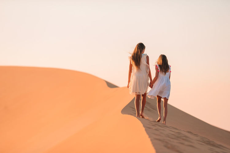 REAR VIEW OF WOMEN WALKING ON SAND DUNE IN DESERT