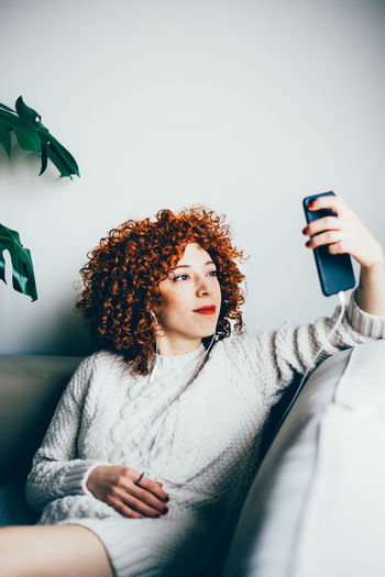 Smiling woman taking selfie while sitting on sofa at home
