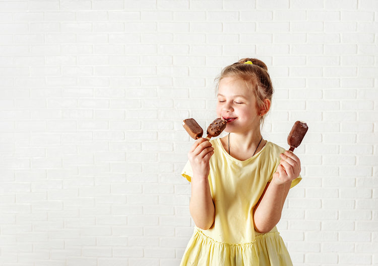 Cheerful smiling girl eating ice cream against wall