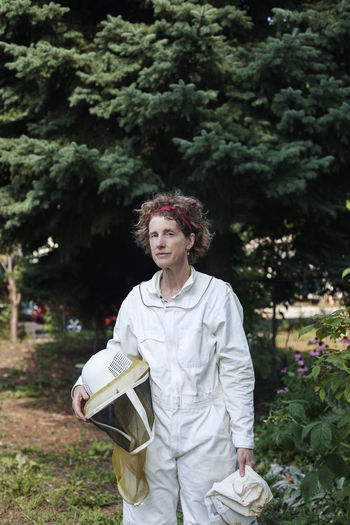 Portrait of confident senior beekeeper wearing protective suit standing on field