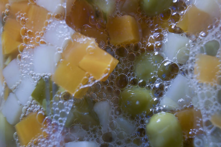 Macro shot of chopped vegetables in a jar with carrot, green peas amongst foam and bubble