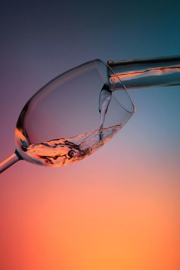 Close-up of water pouring in wineglass from test tube during sunset
