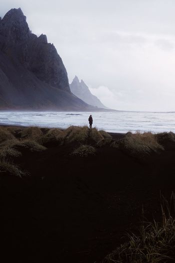 Person standing on shore at beach against sky