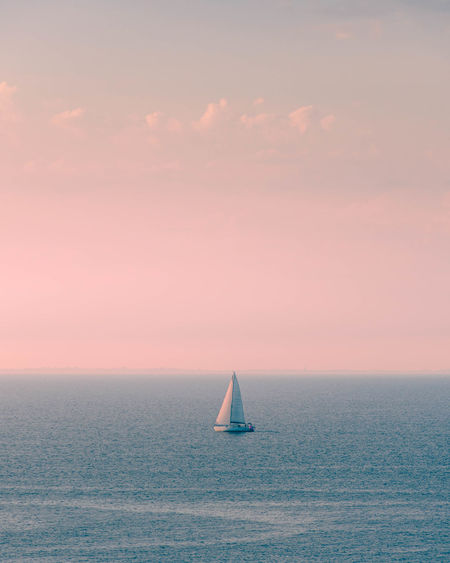 Tranquille and minimalistic sunset above the sea with a sailboat.