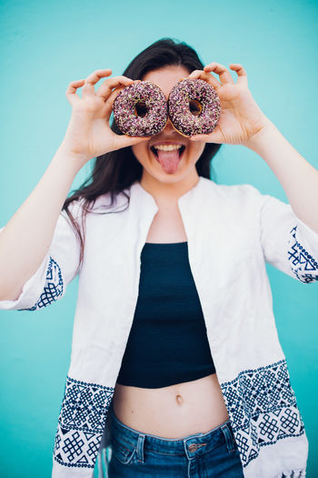 Portrait of young woman holding donuts while standing against blue background