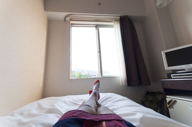 Low section of woman resting on bed against window