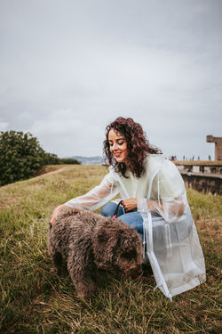 Woman with dog crouching on grass against sky