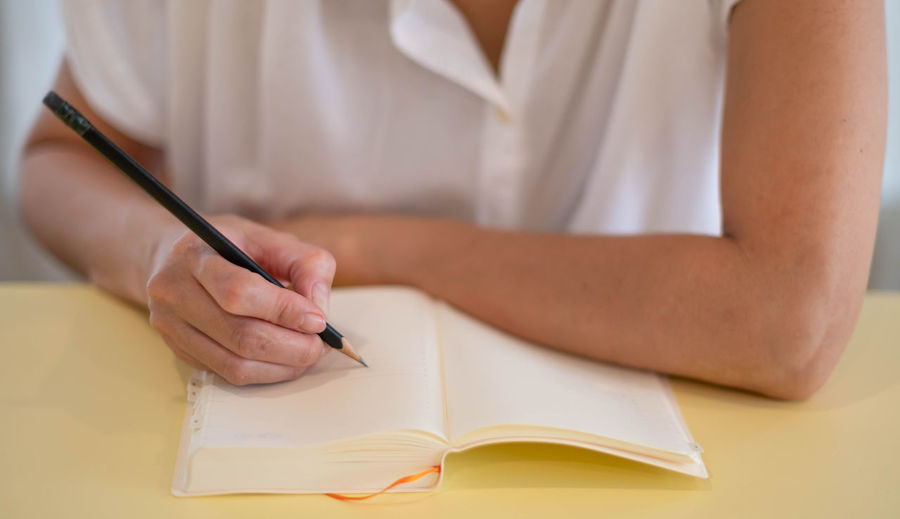 Midsection of woman writing in book at table