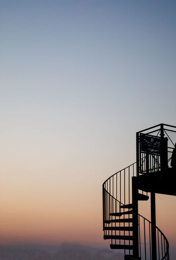 Silhouette staircase by sea against clear sky during sunset