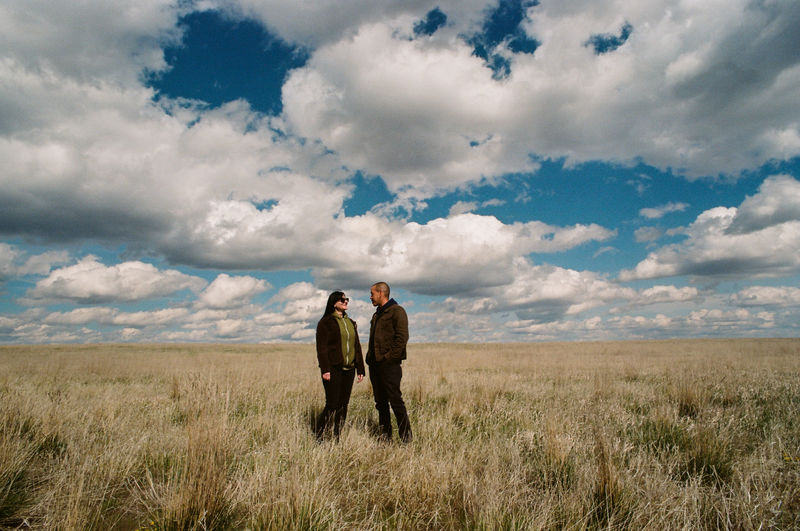 Couple standing on grassy field against cloudy sky
