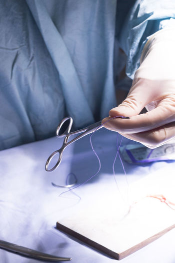 Midsection of doctor holding thread with surgical scissors at hospital