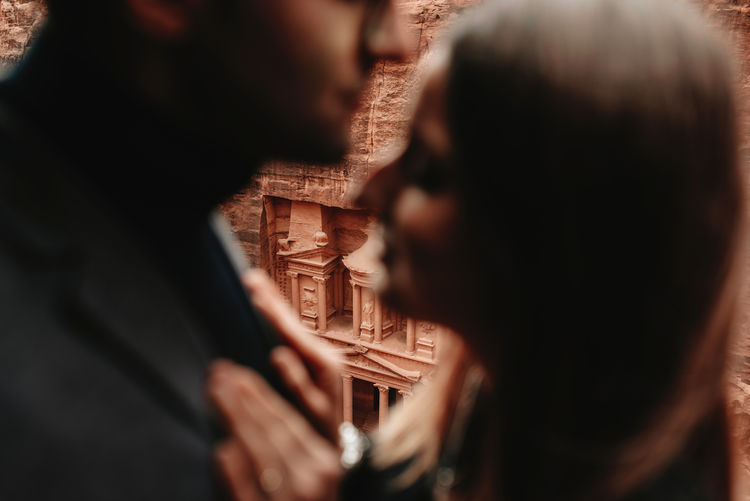 From above blur of young ethnic male traveler in stylish outfit and girlfriend while they hug with amazing view of al khazneh temple, petra, jordan