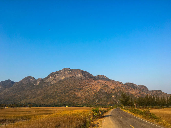 Scenic view of road by mountains against clear blue sky