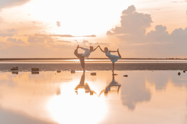 Real people stand in yoga assanas on the seashore at dawn